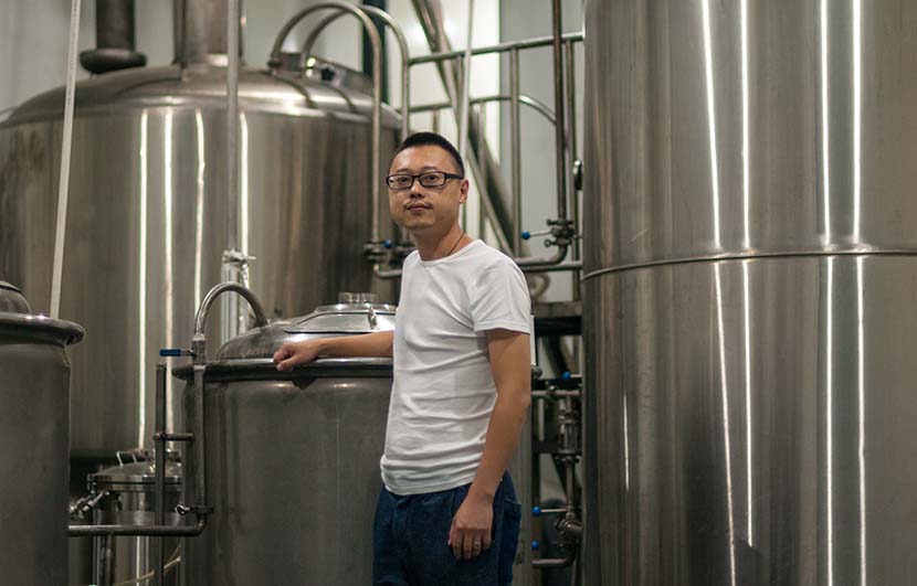 Wang Rui poses with his original 200-liter brewing system, with his new 2,000-liter apparatus in the background, Chengdu, Sichuan province, Oct. 9, 2016. Courtesy of Mark Andrews