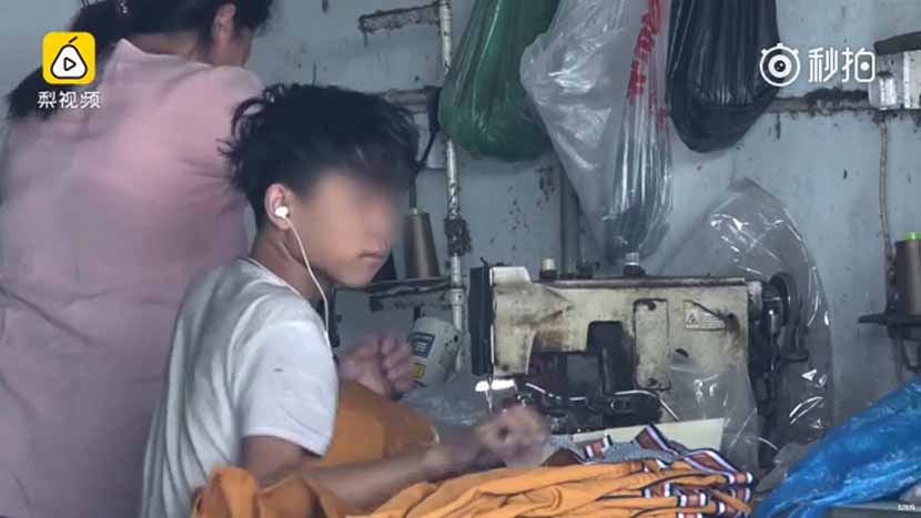 A screenshot from a video news report shows a young boy working at a clothing workshop.
