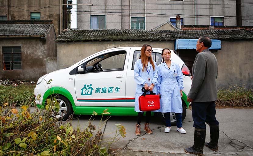 Two family doctors talk with a local resident in front of an electric car that is specially used to take doctors to villages, Jinshan District, Shanghai, Oct. 31, 2016. IC