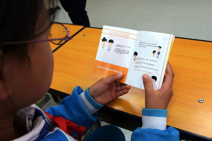 A female student reads a booklet about student safety at an elementary school in Beijing, Oct. 20, 2014. IC