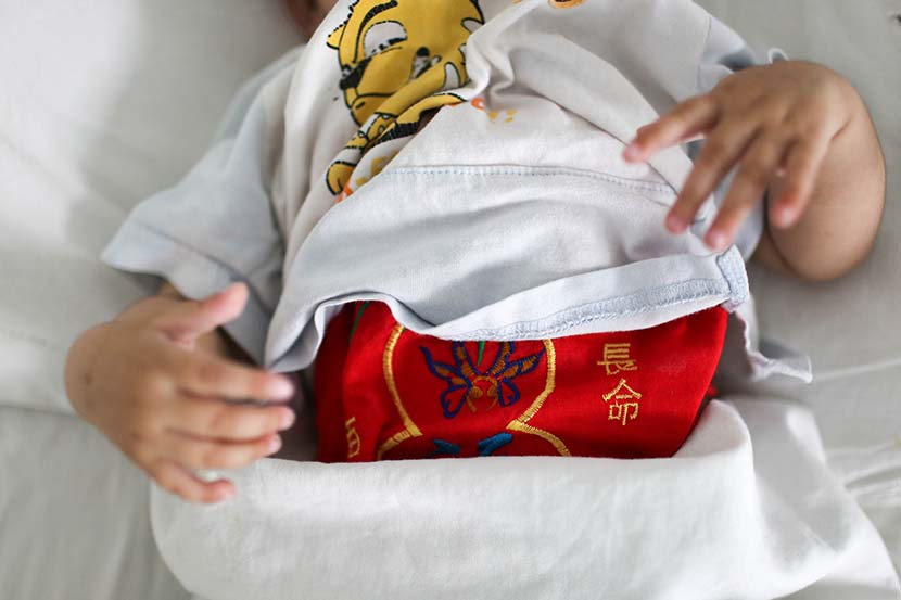 An abandoned infant girl lies on a hospital bed in Jinan, Shandong province, June 14, 2014. The cloth wrapped around her stomach reads ‘live a long life.’ Quan Yi/Sixth Tone