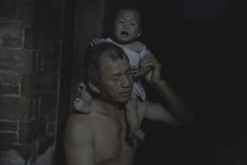 Jin Chengyue holds his baby grandson on his shoulder at home in Paizhouwan Township, Hubei province, Aug. 7, 2016. Zhou Pinglang/Sixth Tone