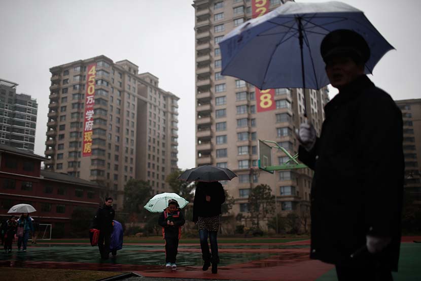 Parents pick up their kids from school as advertisements for ‘xuequfang,’ or school district apartments, hang on the high-rise buildings in the background, Shanghai, Feb. 17, 2014. Yang Yi/Sixth Tone