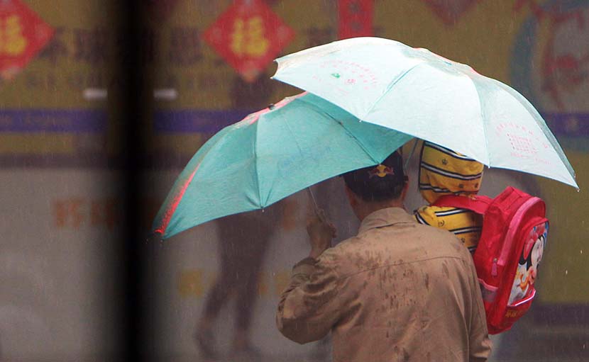 A father takes his son to an English training center in the rain in Nanjing, Jiangsu province, March 29, 2014. VCG