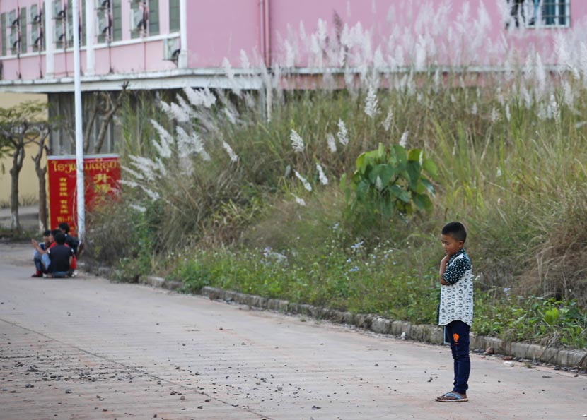 Wang Chao’s younger brother stands in the street, while migrant workers gather nearby in Boten, Laos, Nov. 19, 2016. Jia Yanan/Sixth Tone