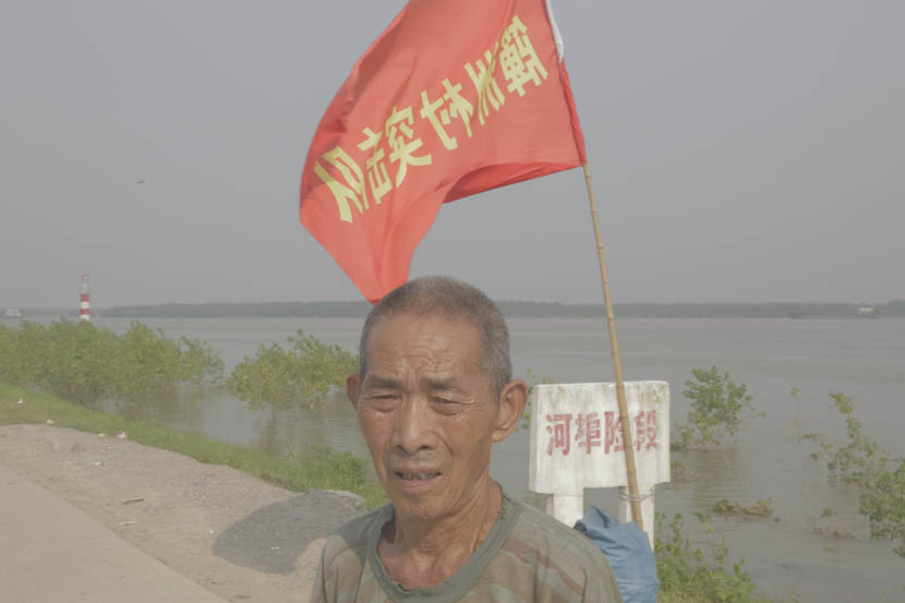 A man stands guard on the embankment in Paizhouwan Township, Hubei province, July 27, 2016. Zhou Pinglang/Sixth Tone