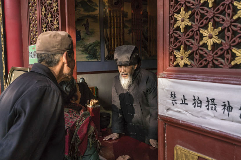 A Taoist monk helps visitors prepare an offering at Louguantai Temple, Tayu Village, Shaanxi province, Jan. 12, 2017. Thomas Cristofoletti for Sixth Tone