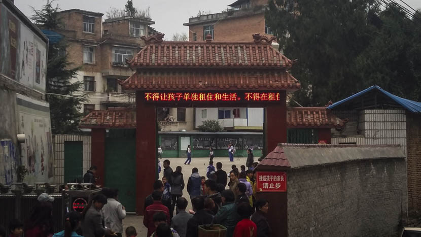 Parents wait to pick up their children from Nayong No. 6 Primary School. An LED banner flashes the message 'Don’t let children live by themselves' in Nayong County, Guizhou province, Nov. 24, 2015. Duan Yanchao/Sixth Tone