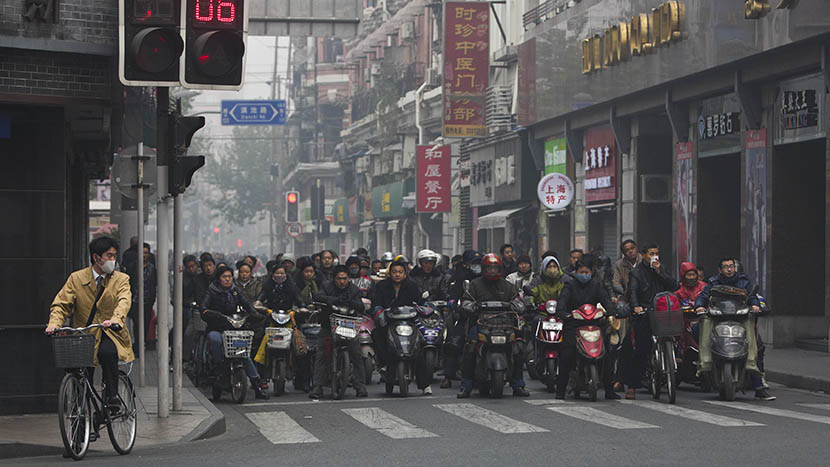 Local residents on e-bikes, motorcycles, and bicycles wait at an intersection on a hazy day in downtown Shanghai, Dec. 6, 2013. Aly Song/Reuters