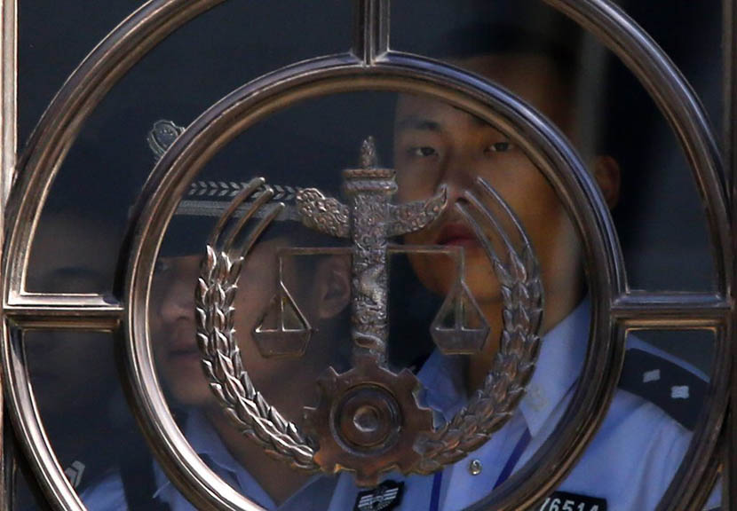 A policeman stands next to a glass door at the Jinan Intermediate People’s Court, Shandong province, Aug. 21, 2013. Carlos Barria/Reuters