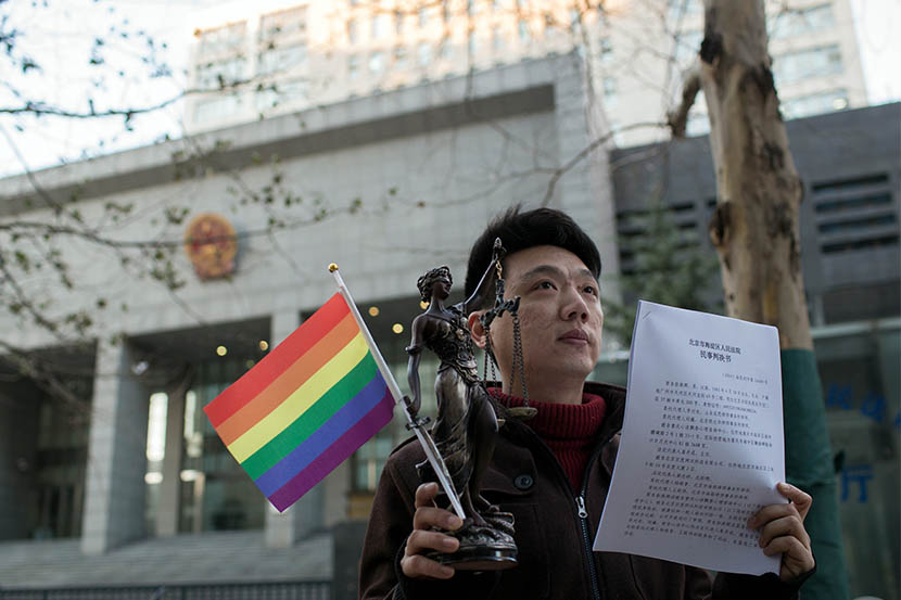 Yang Teng holds a Lady Justice statue and a rainbow flag as he shows the court verdict in front of the Haidian District People's Court, Beijing, Dec. 19, 2014. Yang had successfully sued a clinic that carried out electroshock therapy on him. Xiao Muyi/IC