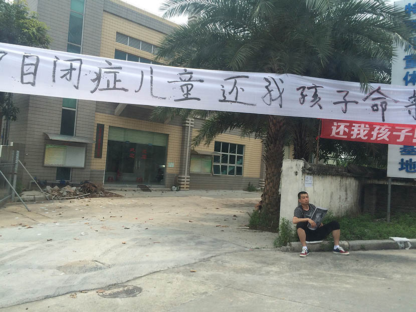 Jia Jia’s father sits holding his son’s photo under a banner that reads ‘I want my son back’ at the entrance to the autism rehabilitation center in Guangdong, Guangzhou province, May 2, 2016. Da Ba for Sixth Tone