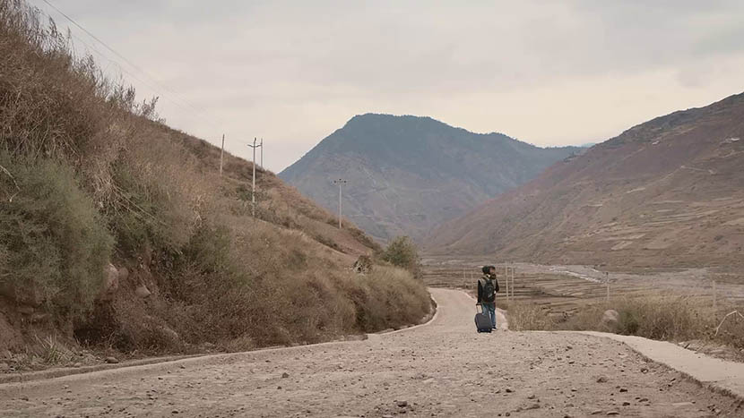 A still from ‘The Verse of Us’ shows poet worker Jike Ayou carrying a young child as he leaves his hometown for manual work. Courtesy of MeDoc.