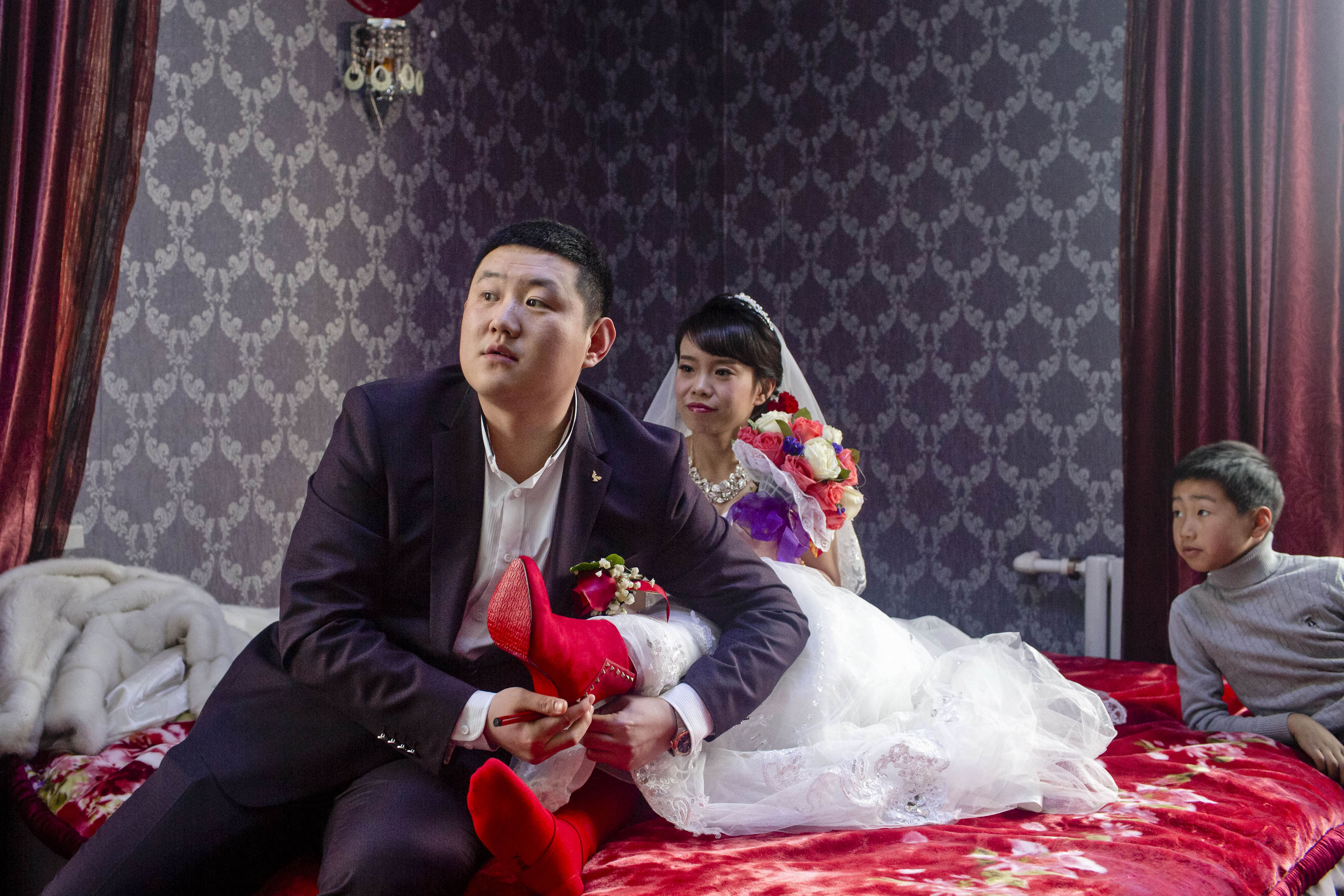 Following the local tradition, Zhang Tianqi helps his wife-to-be put on red high heels before their wedding, Shuangyashan, Jan. 27, 2016. The couple married despite growing insecurity surrounding Zhang’s job. Zhou Pinglang/Sixth Tone