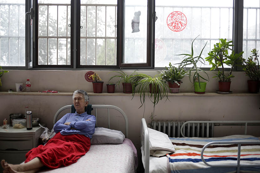 A woman rests in bed at the Songtang Hospice, Beijing, July 19, 2016. The plants by the window were donated by hospice volunteers. Han Meng/Sixth Tone