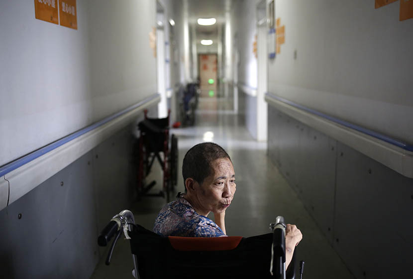 A woman sits in a wheelchair in the hallway of Songtang Hospice, Beijing, July 19, 2016. Han Meng/Sixth Tone