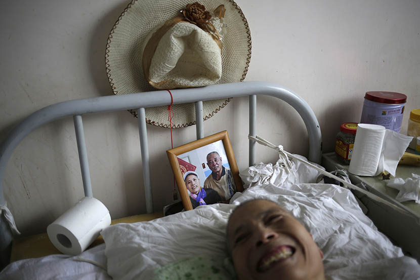 A woman lies in bed with a photo of her husband behind her at Songtang Hospice, Beijing, July 19, 2016. Her husband visits the hospice every day. Han Meng/Sixth Tone