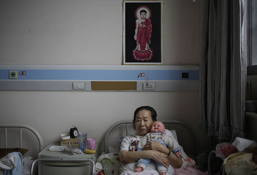 A woman holds a doll donated by a hospice volunteer at Songtang Hospice, Beijing, July 19, 2016. Han Meng/Sixth Tone