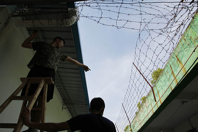Two men install barbed wire fencing to prevent students from escaping a military-style internet addiction treatment center in Huizhou, Guangdong province, Aug. 18, 2016. Chen Weibin/ Nanfang Metropolis Daily/VCG