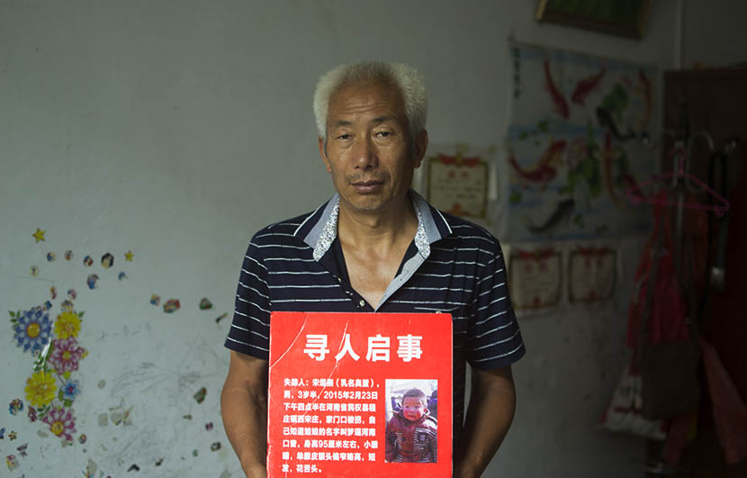 Song Xianzhong poses at home with the missing persons notice of his grandson Song Yuxi, Songzhuang, Henan province, Aug. 1, 2016. Owen Churchill/Sixth Tone