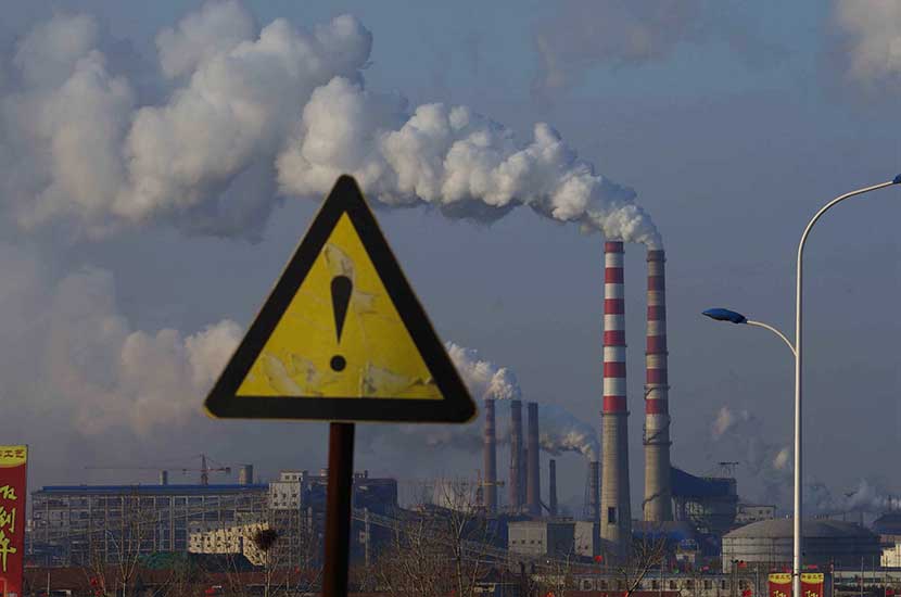 A warning sign with chimneys visible in the background, Rizhao, Shandong province, Feb. 19, 2015. Guo Lei/VCG
