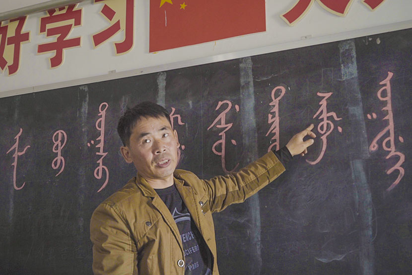 Shi Junguang talks pupils at the Sanjiazi Manchu Elementary School through a Manchu phrase, which reads ‘Sanjiazi Manchu Elementary School welcomes you,’ Qiqihar, Heilongjiang province, May 10, 2017. Tang Xiaolan/Sixth Tone