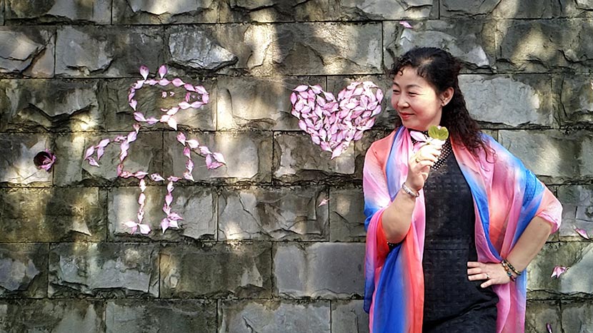 A woman poses for a photo next to an outline of Peppa Pig made from flower petals at a park in Liuzhou, Guangxi Zhuang Autonomous Region, April 1, 2018. Zhang Cunli/IC