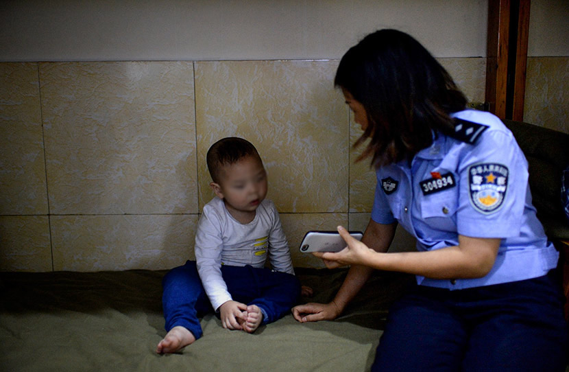 A police officer shows her mobile phone to a child abandoned by relatives at a police station in Chongqing, May 4, 2018. Chongqing Evening Post/VCG