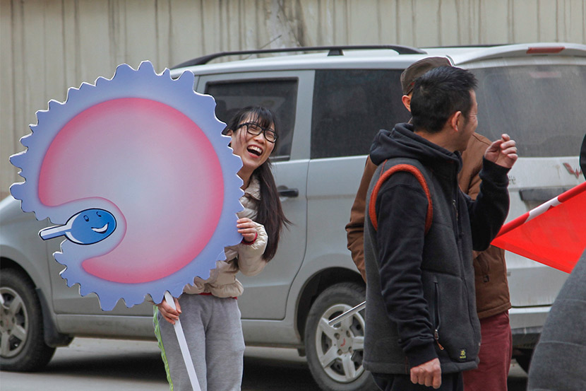 A woman holds a sign showing an egg and sperm in Zhengzhou, Henan province, March 23, 2016. IC