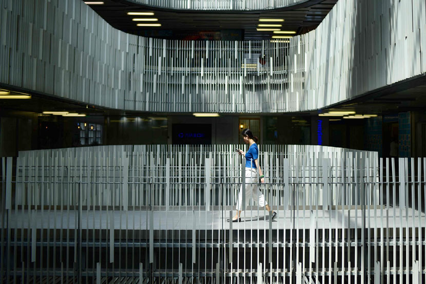 A woman looks at her mobile phone as she walks through a building in Beijing, May 8, 2018. Wang Zhao/AFP/VCG