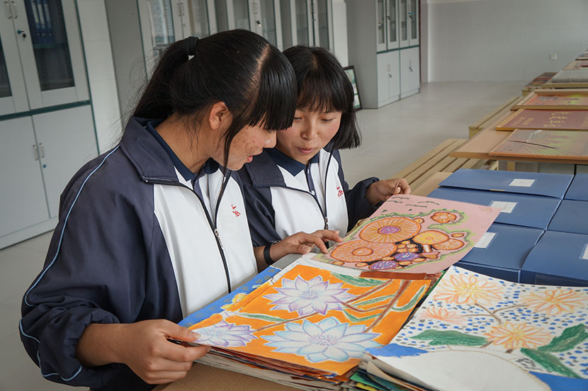 Zhi Zhengjiao (left) and Chang Ranran look at works of art created by their classmates at Nanjian No. 2 Middle School in Nanjian Yi Autonomous County, Yunnan province, March 22, 2018. Fan Yiying/Sixth Tone