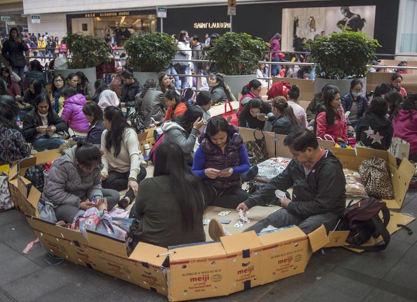 Filipina workers sit on cardboard boxes playing cards on their day off in Hong Kong, Feb. 18, 2018. Andrew Caballero-Reynolds/VCG
