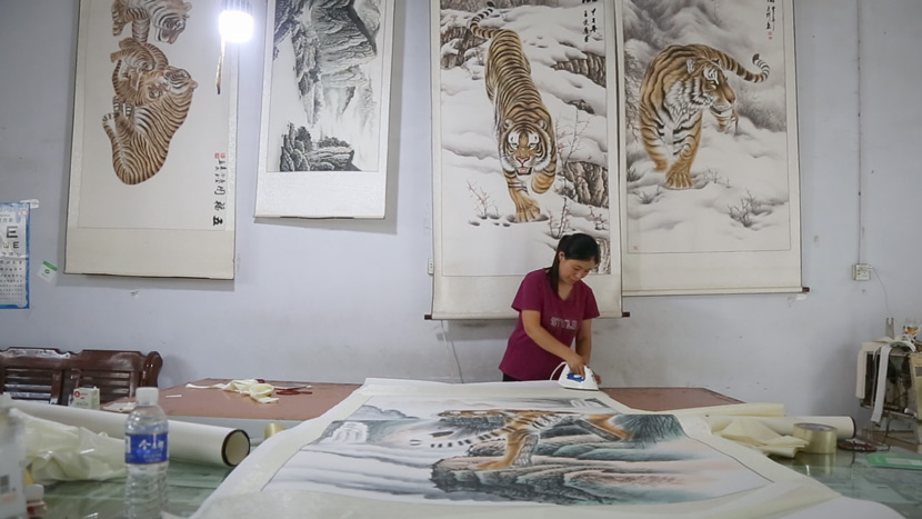 Wang Ximei irons the edges of a painting in Wanggongzhuang Village, Minquan County, Henan province, July 11, 2018. Liu Jingwen/Sixth Tone