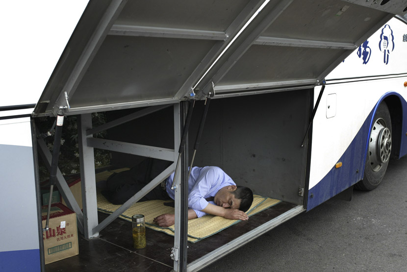 A driver takes a nap inside the luggage compartment of a bus in Nanjing, Jiangsu province, June 6, 2007. Xiao En/VCG