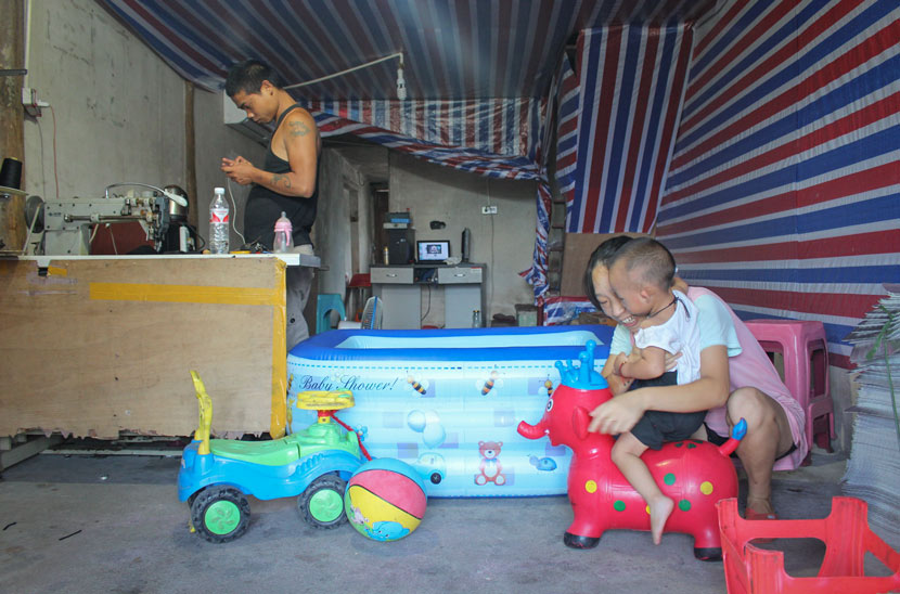 Zhang Yueying plays with her son while her husband stands by a sewing machine at their home in Shi’erdai Village, Zhejiang province, Aug. 4, 2018. Xue Yujie/Sixth Tone