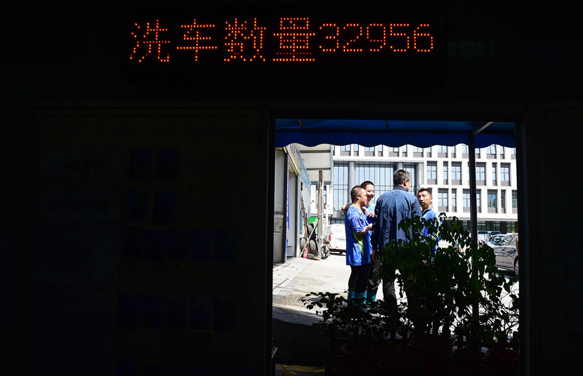 Cao Jun (middle) talks to Xihaner Car Wash employees as a screen counts the number of cars washed, Shenzhen, Guangdong province, April 25, 2018. Liao Jian/VCG