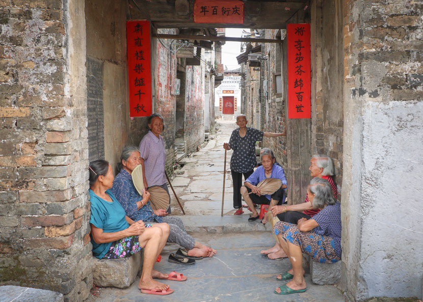 He Yanxin spends her leisure time chatting with elders in the alleyways of Heyuan Village, in Jiangyong County, Hunan province, July 18, 2018. Yin Yijun/Sixth Tone