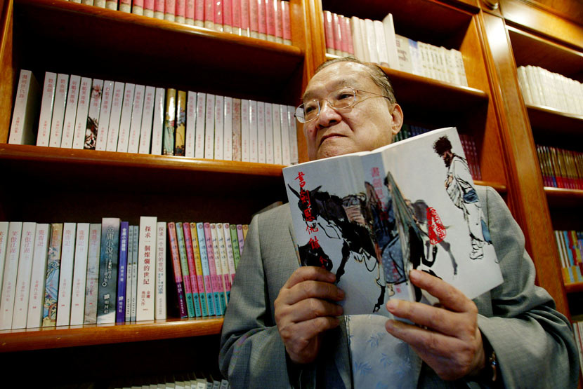 Louis Cha poses for a photo while holding a copy of his novel ‘The Book and the Sword’ in Hong Kong, July 29, 2002. Bobby Yip/Reuters/VCG