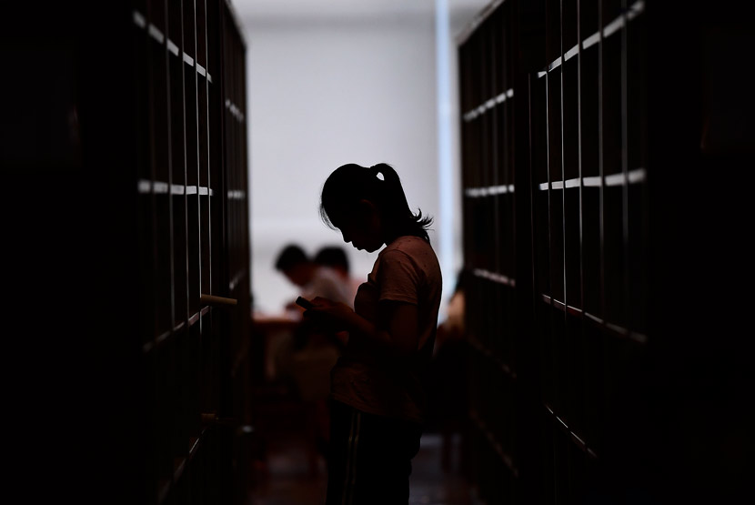 A student stands between book shelves in a university library in Shenyang, Liaoning province, July 5, 2018. VCG