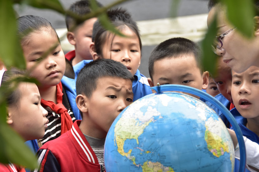 Students look at a world globe on Earth Day at a primary school in Congjiang County, Guizhou province, April 22, 2019. Luo Jinglai/Xinhua