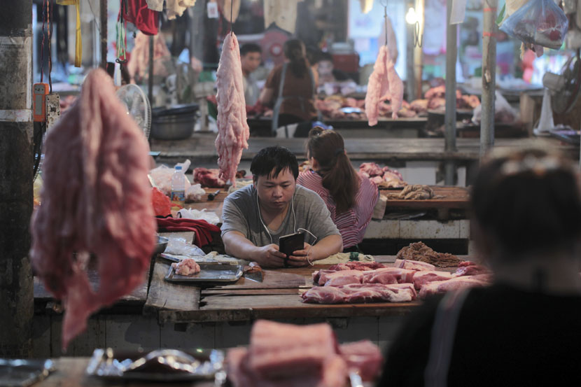 A vendor looks at an electronic device in a meat market in Hekou Yao Autonomous County, Yunnan province, May 3, 2019. Wong Campion/Reuters/VCG