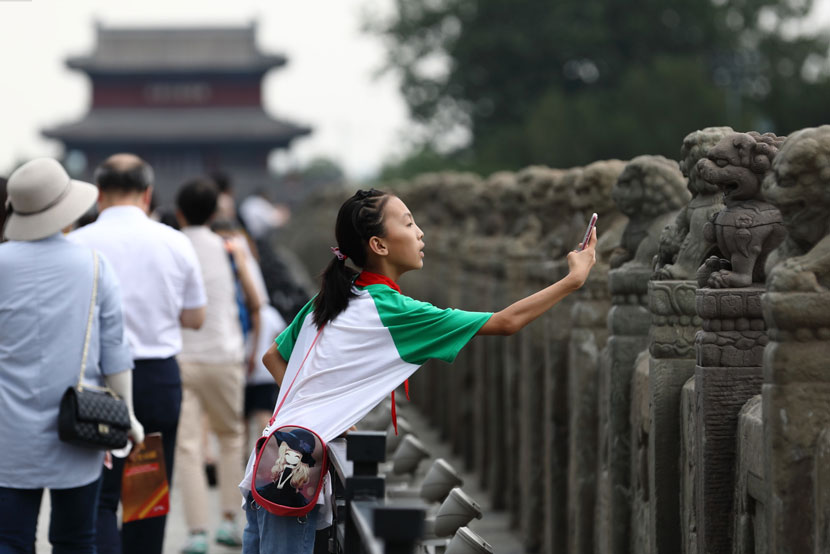 A girl photographs lion statues along the Marco Polo Bridge in Beijing, July 5, 2019. IC