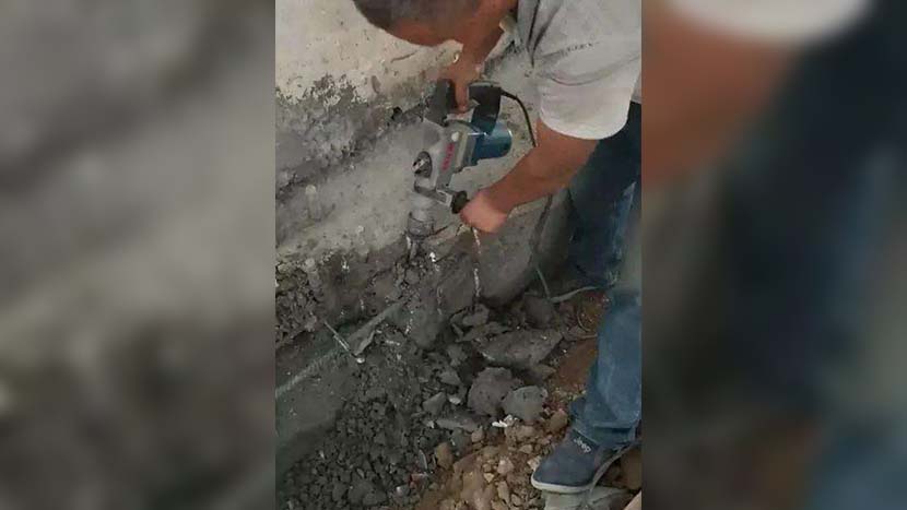 A video screenshot shows a construction worker demolishing the wall of a dormitory built with the allegedly substandard cement at Zhicheng Experimental School in Luyi County, Henan province. @中国青年报 on Weibo