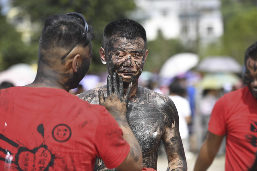 A man smears rice ash onto another during the traditional Hualian Festival in Qiubei County, Yunnan province, July 18, 2019. Members of the Yi ethnic group say the practice is performed to expel evil and express good wishes. Liu Ranyang/CNS/VCG
