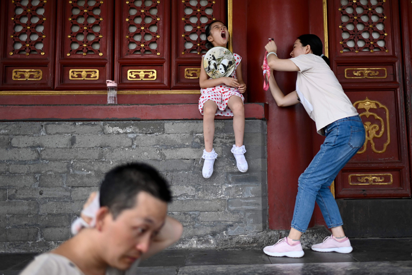 A girl holding a fan yawns while posing for a photo at a park in Beijing, July 22, 2019. The Beijing weather department issued a blue warning on July 22, indicating a heat wave for the coming days. Wang Zhao/AFP/VCG
