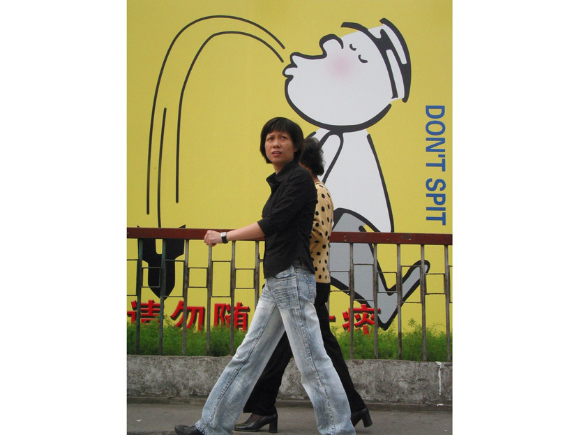 Two people walk past a wall warning against spitting in public, Shanghai, 2003. VCG
