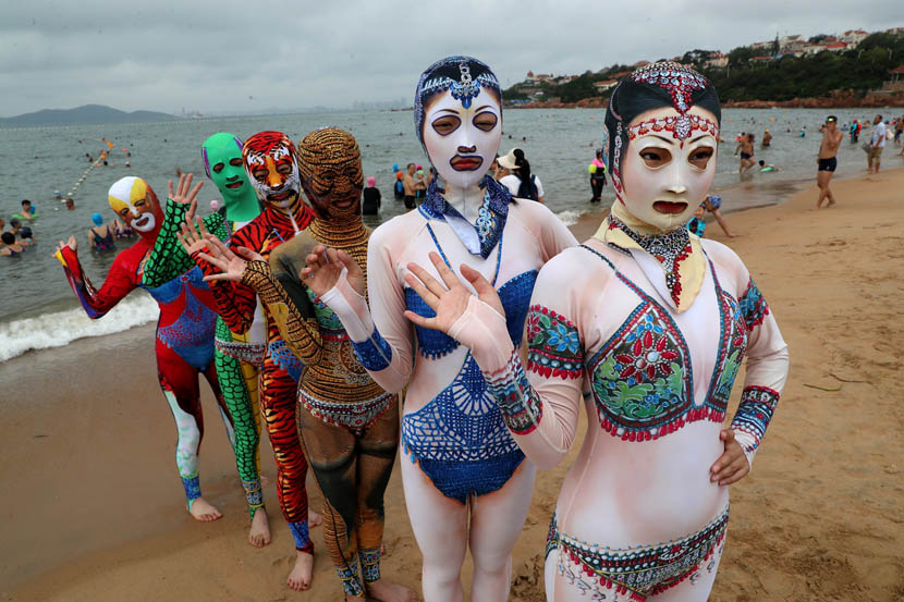 Models wearing colorful, full-body “facekinis” pose for photos on a beach in Qingdao, Shandong province, Aug. 5, 2019. Xu Chongde/VCG