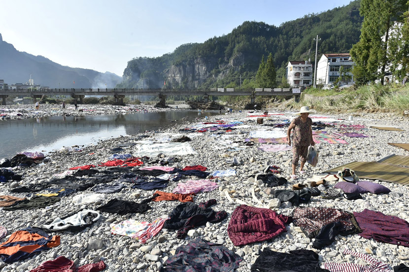 Villagers lay their clothes, sheets, and blankets along the stony banks of a river to dry after floodwaters caused by Typhoon Lekima receded in Xianju County, Taizhou, Zhejiang province, Aug. 12, 2019. Zhejiang Daily/VCG