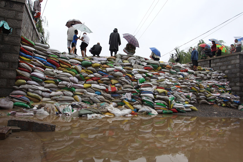 People stand on sandbags piled high to stop the flow of floodwaters caused by Typhoon Lekima in Zhangqiu District, Jinan, Shandong province, Aug. 13, 2019. VCG