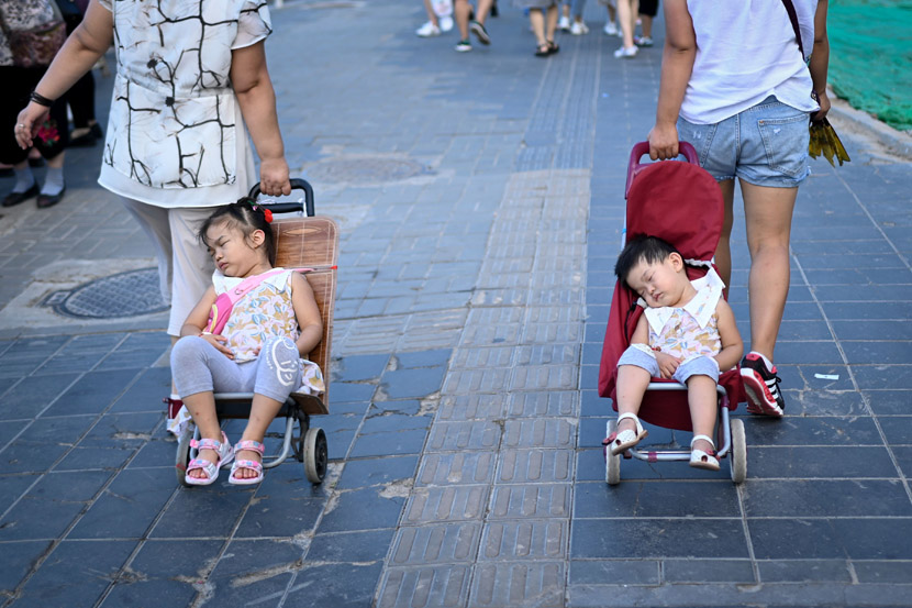Two women pull their sleeping children in strollers as they walk along a road in Beijing, Aug. 13, 2019. Wang Zhao/AFP/VCG